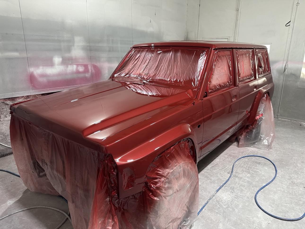 A red 4WD masked up in plastic mid-respray inside the Easy As Refinishing spray booth